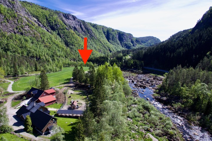 Aerial view of a valley with buildings, a river, and an arrow pointing to a specific location.