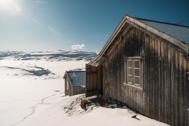 Wooden cabin in snowy landscape with clear sky and sunlight.