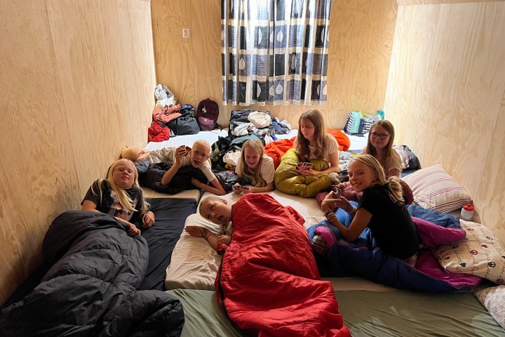 Group of children in sleeping bags on the floor of a wooden room.
