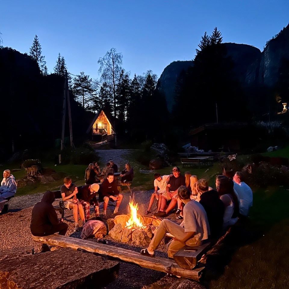 Group of people sitting around a campfire in a mountainous area at dusk.
