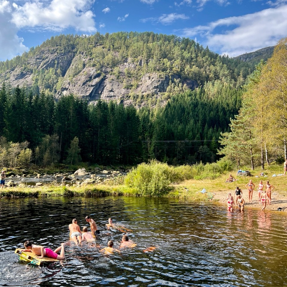 People swimming in a lake with forested mountains and blue sky background.