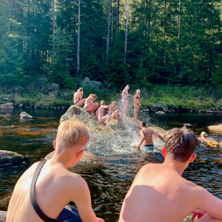 People sitting and swimming in a forest river under sunlight.