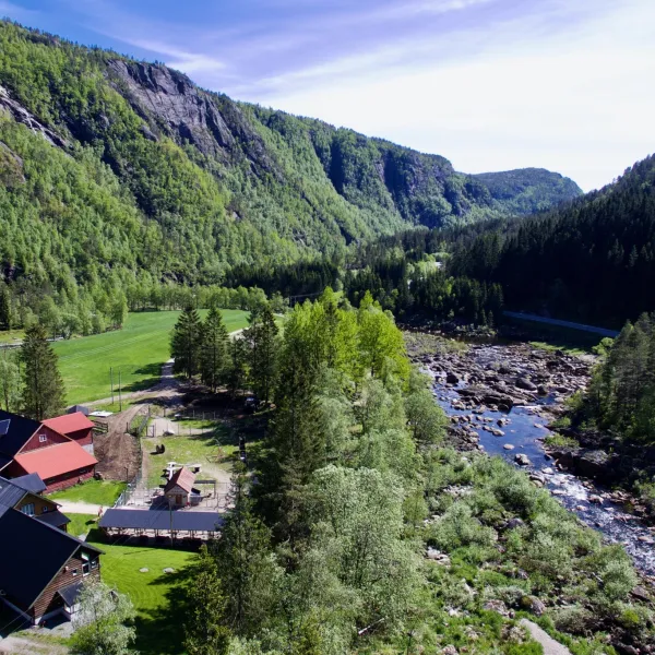 Aerial view of a valley with green hills, a river, and several houses with red roofs.
