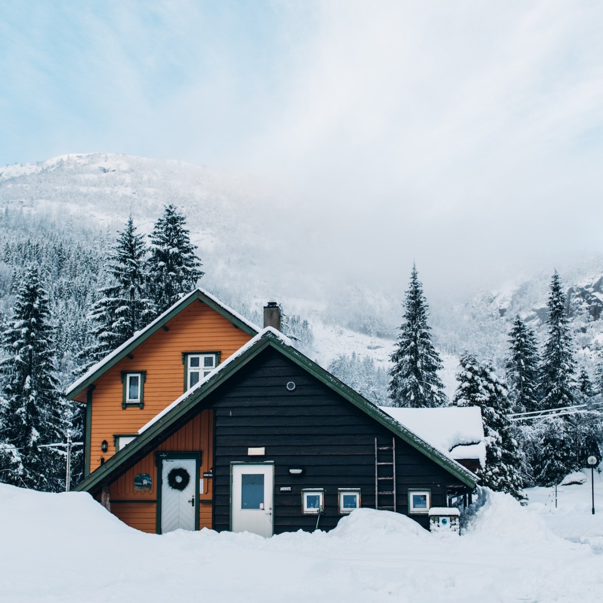 A-frame cabin in snowy landscape with forest and mountain backdrop.