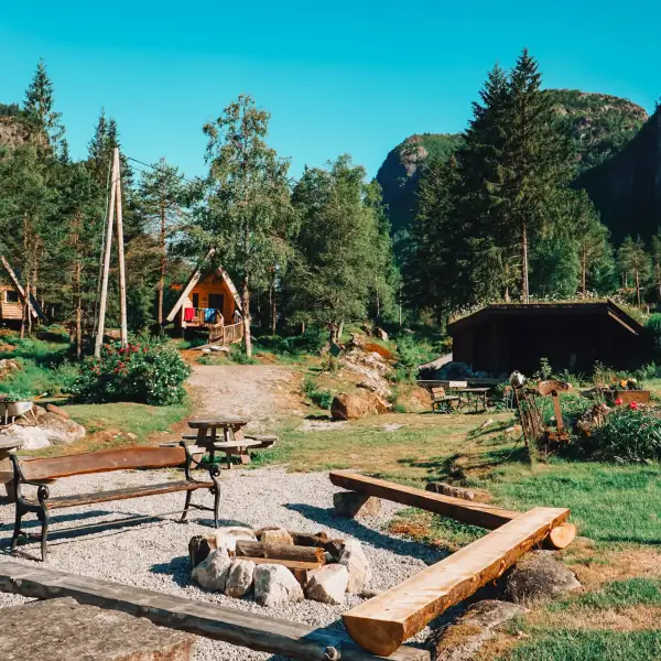 Wooden benches around a fire pit, cabins in a forested mountain setting.