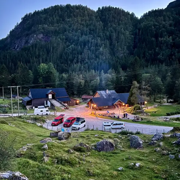 Scenic view of cabins, cars, and forested hills at dusk.