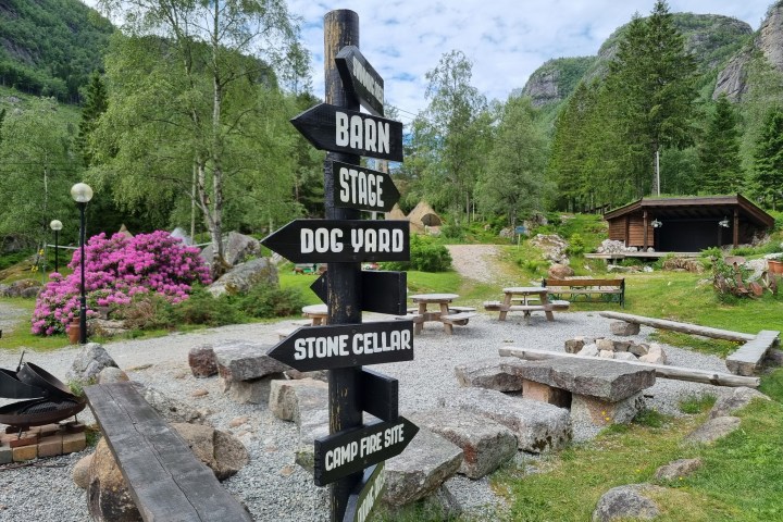 Wooden signpost with directions, garden setting, trees, and picnic tables.