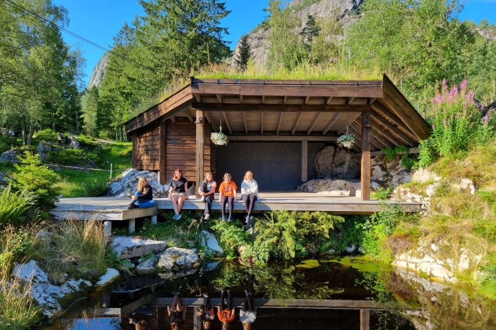 People sitting on porch of wooden cabin by a pond in nature.